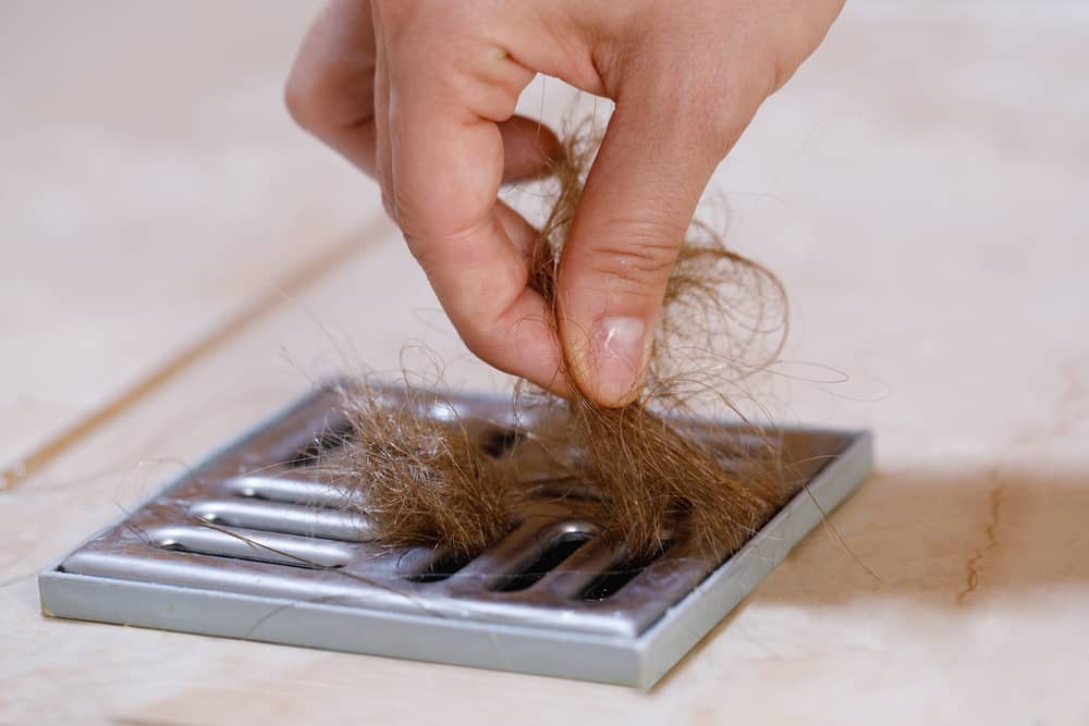 Woman Removing Hair Clump from the Shower Drain
